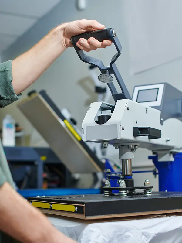Mann bedient Siebdruckmaschine um T-Shirt mit diesem Druckverfahren zu bedrucken